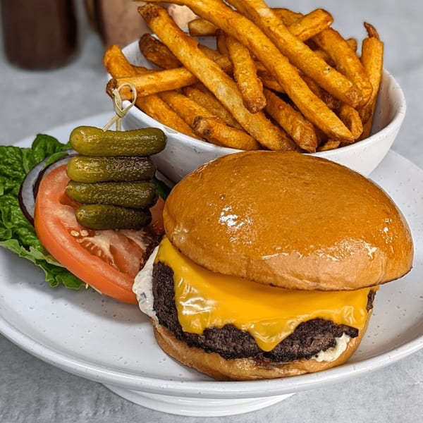 Cheeseburger with lettuce, tomato, onion, pickles, and a side of golden french fries.