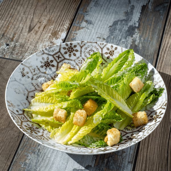 Fresh Caesar salad with crisp romaine lettuce and golden croutons in a decorative bowl on a wooden table.