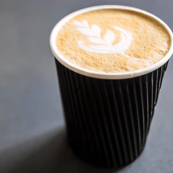 Close-up of a black ripple-textured coffee cup with latte art on a gray surface.