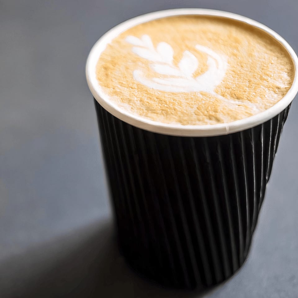 Close-up of a black ripple-textured coffee cup with latte art on a gray surface.