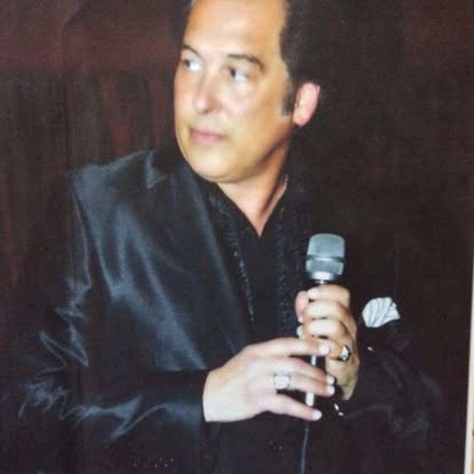 Craig holding a microphone in a black suit