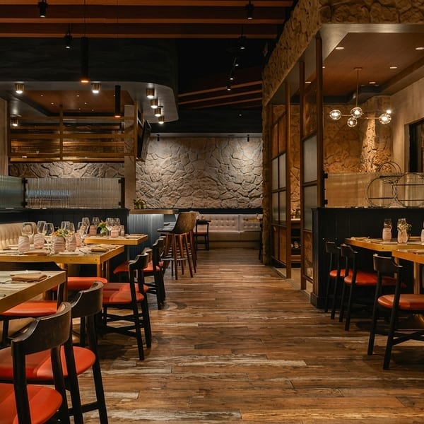 Elegant restaurant interior with set tables, red chairs, banquette seating, and stone walls under warm lighting.
